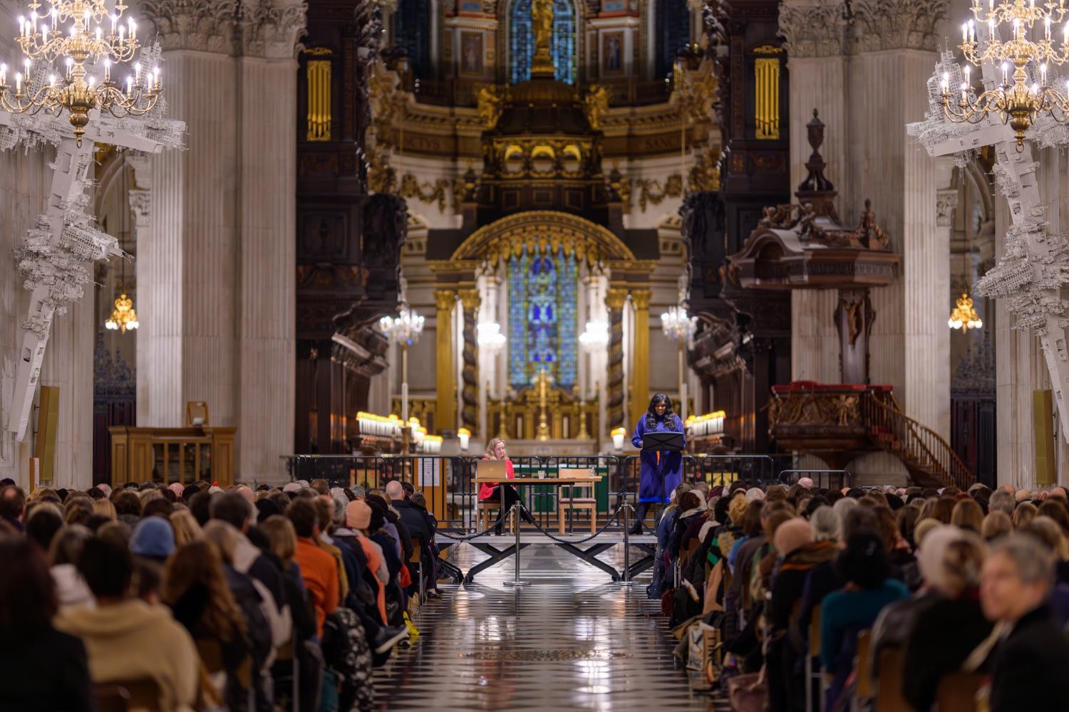 a large audience sit in front of a stage with two speakers in st paul's cathedral