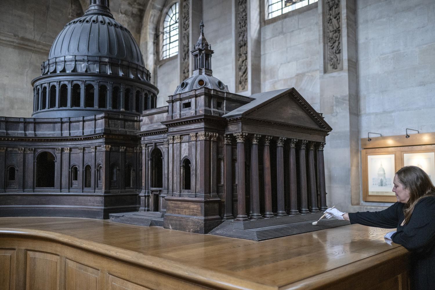 a wooden model of the cathedral made by Christoppher Wren with conservator cleaning the base wearing white gloves