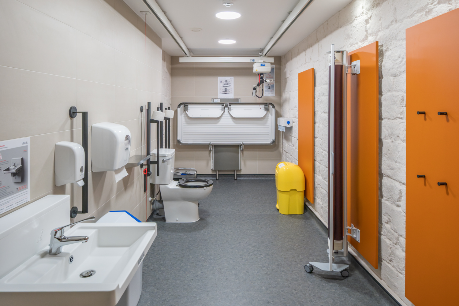 An interior photos of a changing places toilet featuring a height adjustable sink, toilet, hoist and changing table.