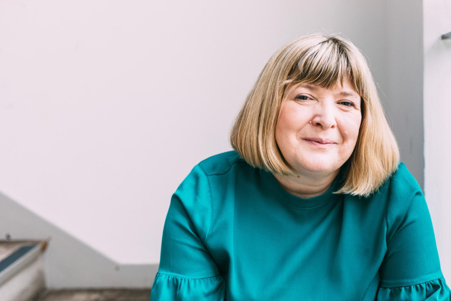 A woman with straight blond hair in a neck length bob wearing a deep green shirt