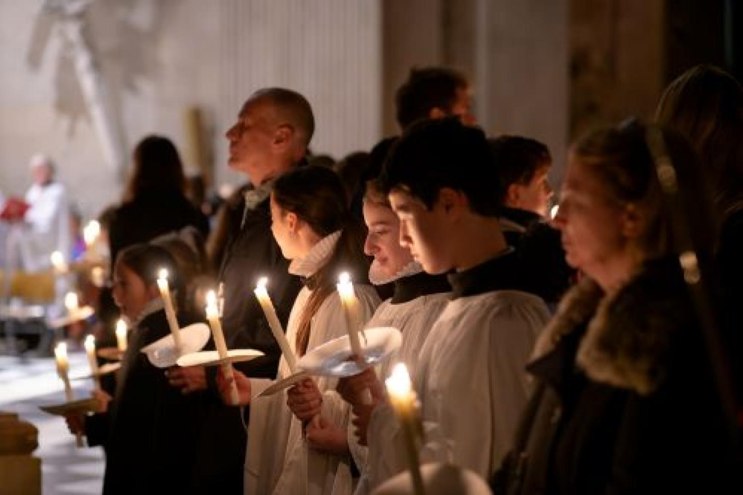 Choristers and adults stand holding lit candles at Advent
