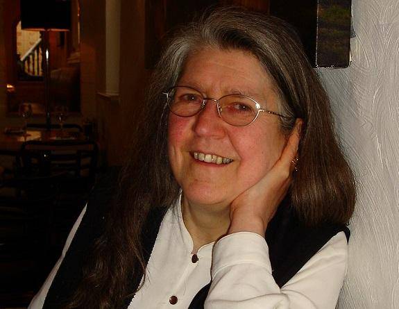 Janet Tollington leans her elbow on a table and with her hand under her chin smiles towards the camera