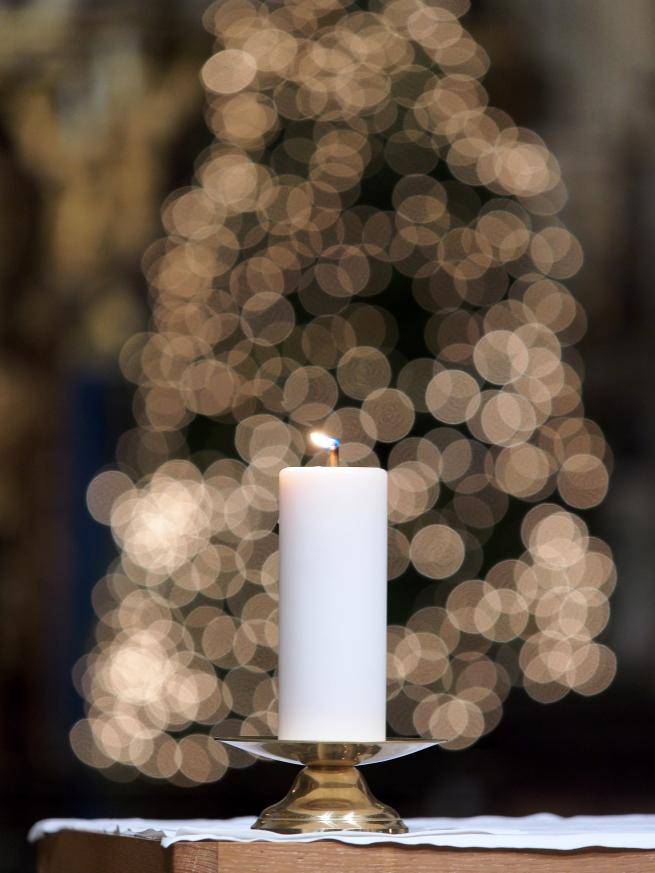 A lit candle with a Cathedral Christmas tree in the background