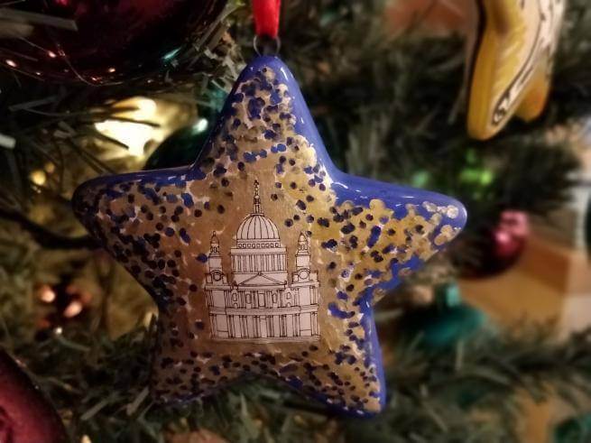 A blue and gold star Christmas decoration hangs from a Christmas tree