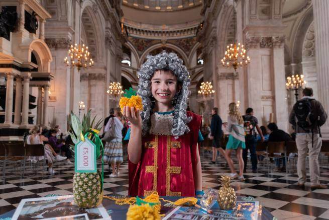 A young boy, dressed as Christopher Wren, holds a pineapple inside the Cathedral