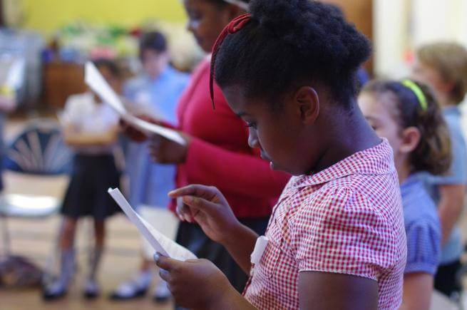 A young black girl in a red and white checked school summer dress is intently reading sheet music