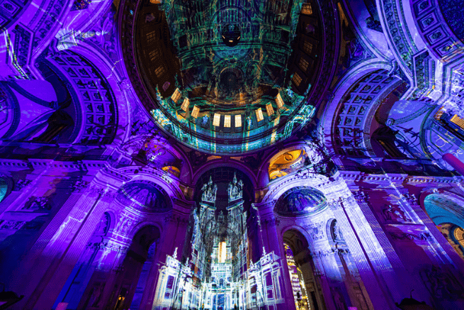 The dome and south transept lit with purple projections, featuring an image of the Old St Paul's Cathedral.