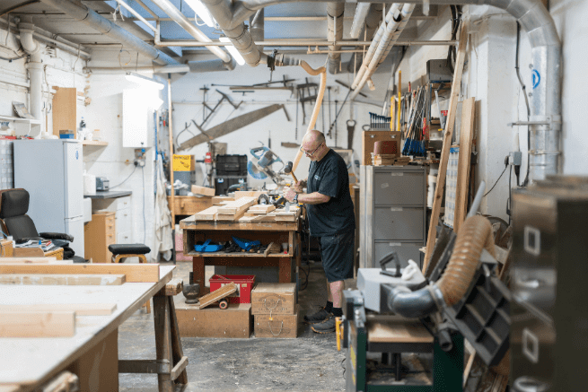 Male carpenter in a workshop standing in front of a workbench with wood and tools