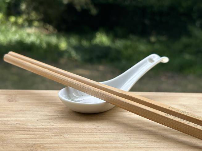 two wooden chopsticks sit on a chinese soup spoon on a wooden table in a garden