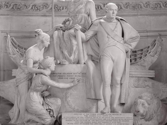 The memorial to Lord Admiral Howe on the Cathedral floor. A white marble statue depicting Howe surrounded by classical style female figures, a boat and a lion.