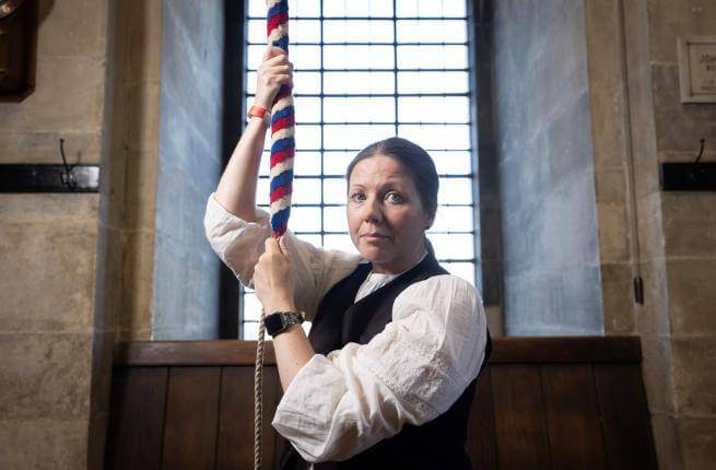 A bereaved mother faces the camera and while pulling a bell rope