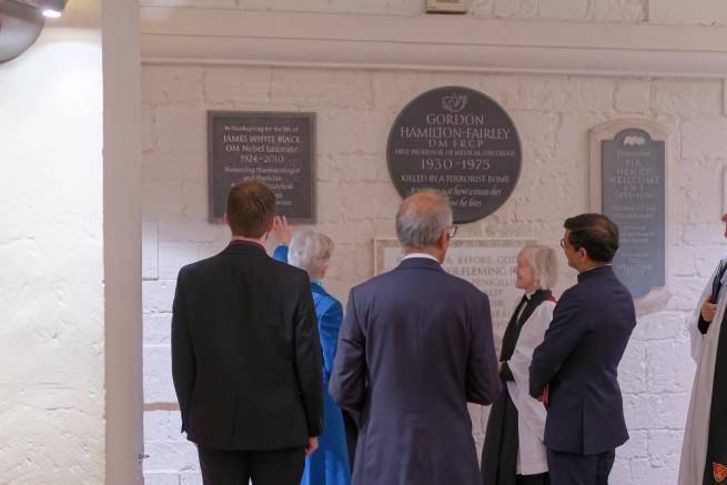 A group of people stand in front of a memorial plaque in the Crypt.