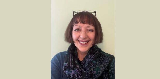 Carys has short brown hair, wears glasses on her head and a blue jumper with a blue scarf