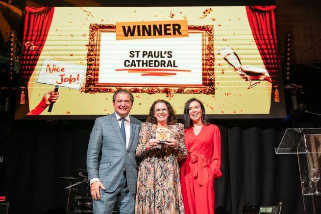Kim Newland holds award with presenters in front of a screen that says 'Winner: St Paul's Cathedral: Best Cultural Experience'