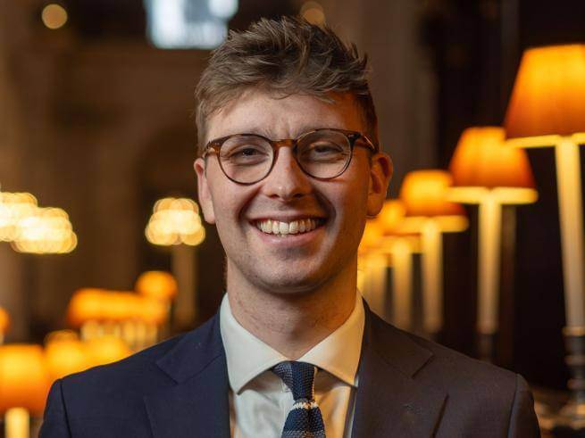 George Cook smiling, wearing glasses and a blue suit jacket and white shirt