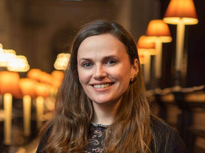 Laurel Neighbour smiling, with brown curly hair, wearing a black jacket and a floral patterned blouse