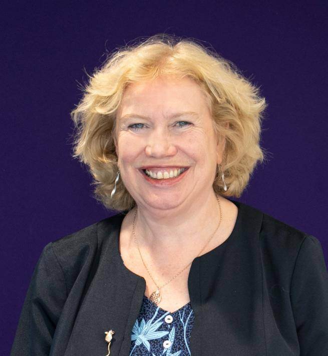 Meg Munn, a white woman with blonde hair, photographed in front of a navy blue background.