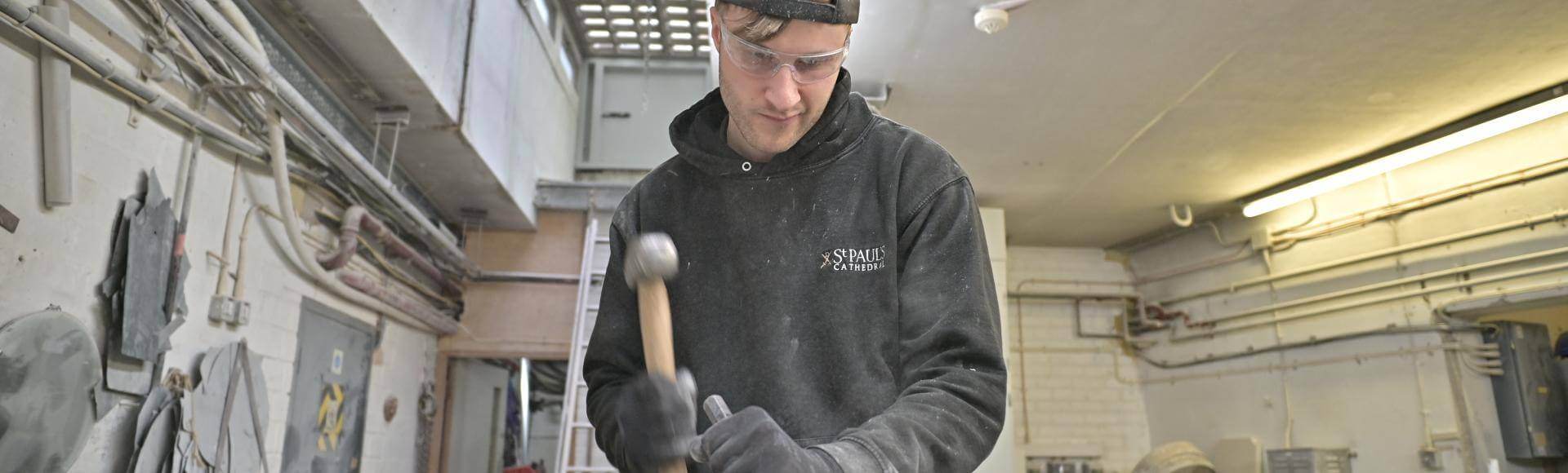 stonemason using a hammer and chisel to carve a large stone inside a workshop