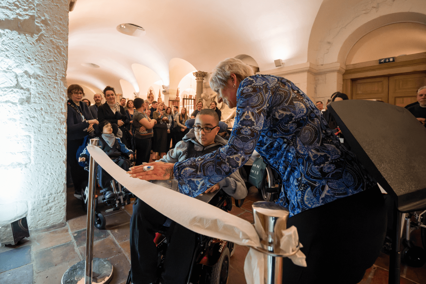 A child in a wheelchair cutting a toilet paper ribbon to open the Changing Places toilet