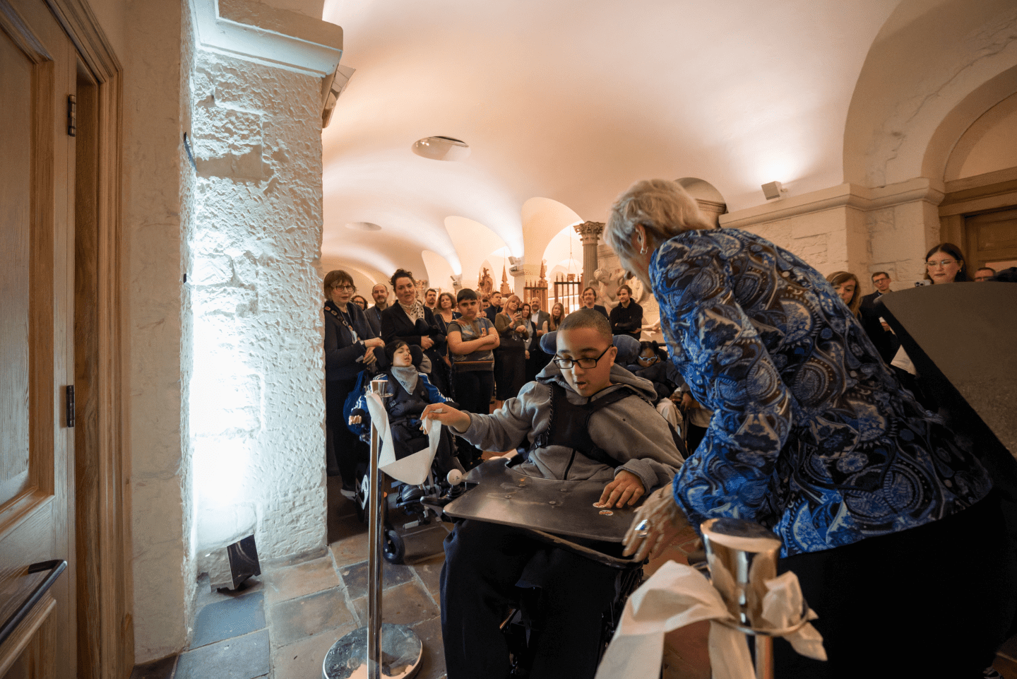 A child in a wheelchair cutting a toilet paper ribbon to open the Changing Places toilet