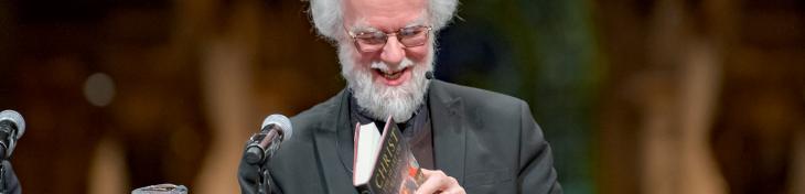 Rowan Williams smiling as he leafs through his book at an event at St Paul's Cathedral