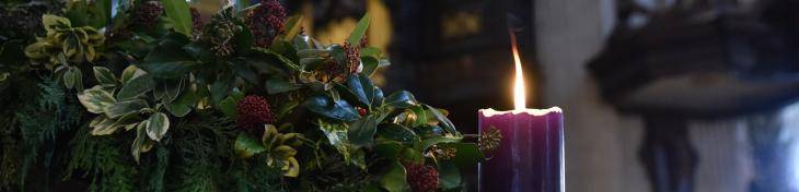 An image of a lit purple candle in the Advent wreath with the organ pipes in the background