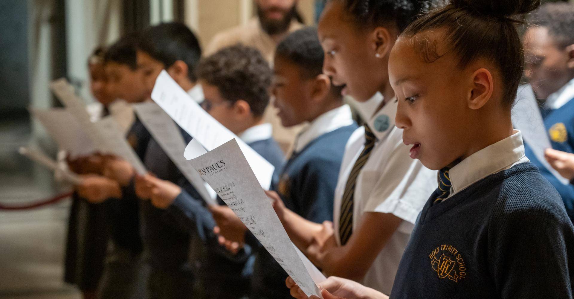 Girls and boys in school uniform sing from sheet music.