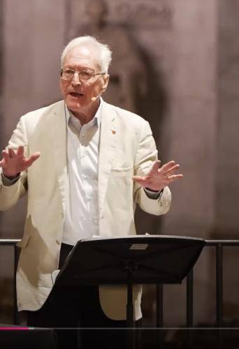 Diarmaid MacCulloch, a white man with white hair and glasses, wearing a cream linen jacket over a white shirt, stands at a lectern in St Paul's Cathedral