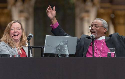 Bishop Curry raises his arms and Paula Gooder laughs alongside on the stage at an event at St Paul's Cathedral