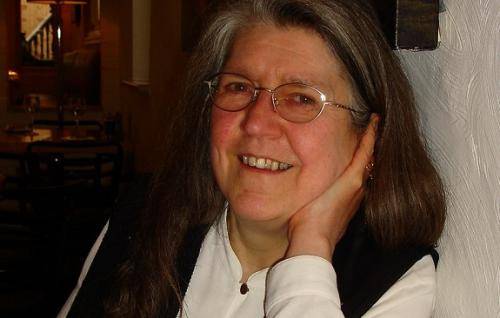 Janet Tollington leans her elbow on a table and with her hand under her chin smiles towards the camera