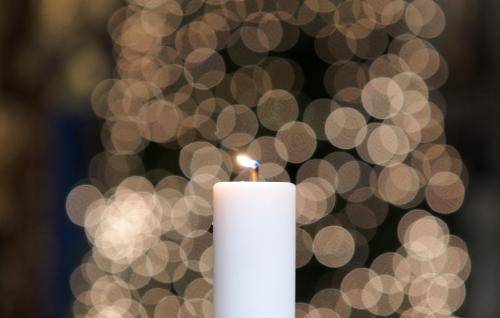 A lit candle with a Cathedral Christmas tree in the background