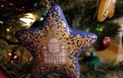 A blue and gold star Christmas decoration hangs from a Christmas tree