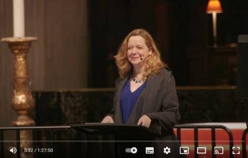 Paula Gooder smiles at the lectern in St Paul's Cathedral. Behind her you can see the front of the quire and one of its lamps and a large white candle on its golden stand.