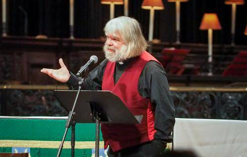 Malcolm Guite stands on the dais at St Paul's Cathedral, hand raised as he speaks, green altar cloth on the altar behind him.