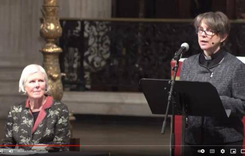 Lucy Winkett speaking from the lectern at St Paul's Cathedral with Marian Partington listening from a table beside her.
