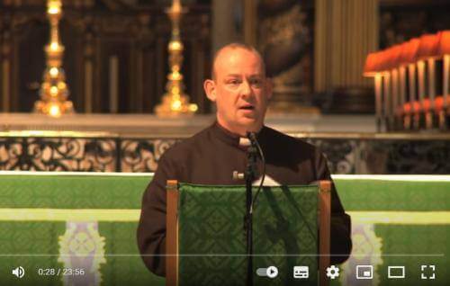 Giles Fraser, a white man in clerical robes, stands behind the lectern at St Paul's Cathedral, a green altar cloth on the altar behind him. 