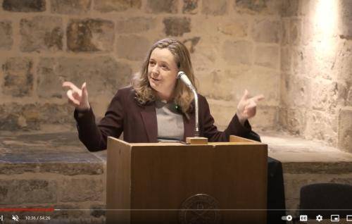 Paula Gooder, a white woman with long blond hair, talking at a lectern in the Wren Suite of St Paul's Cathedral