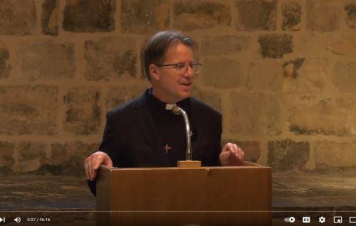 Richard Carter talks from the lectern in the Wren Suite at St Paul's, an exposed brick wall behind him.