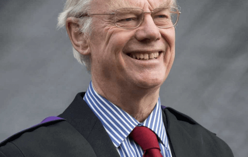 A grey-haired white man with glasses wearing academic robes over a suit and tie.