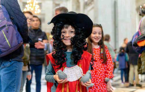 A young child wearing a long black, curly wig and wide brimmed hat, dressed as Christopher Wren.