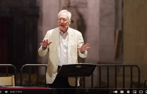 Diarmaid MacCulloch, a white man with white hair and glasses, wearing a cream linen jacket over a white shirt, stands at a lectern in St Paul's Cathedral