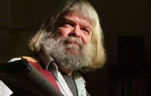 Malcolm is a white man with longish grey hair and a full beard