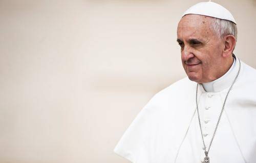Pope Francis stands against a pale background