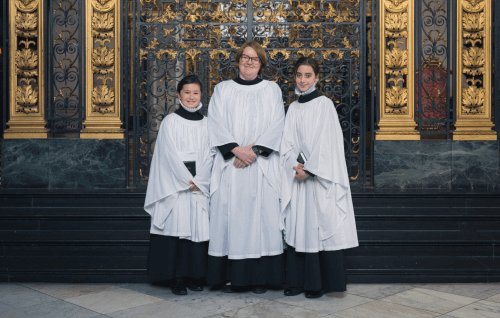 Two girl choristers pose in front of the Dean's Aisle with Carris Jones, Girls' Voices Project Manager.