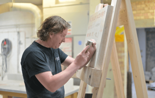 Stonemason carving letters into a flat stone on an easle