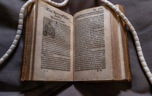 Tyndale Bible open at "The Acts of the Apostles". Long white "snake" weights are visible holding the top right and left corners of paper open. 