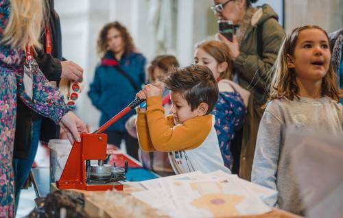 A child pulls down on a large stamp with other children around