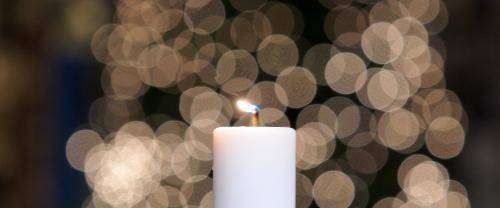 A lit candle with a Cathedral Christmas tree in the background