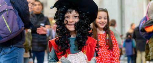 A young child wearing a long black, curly wig and wide brimmed hat, dressed as Christopher Wren.